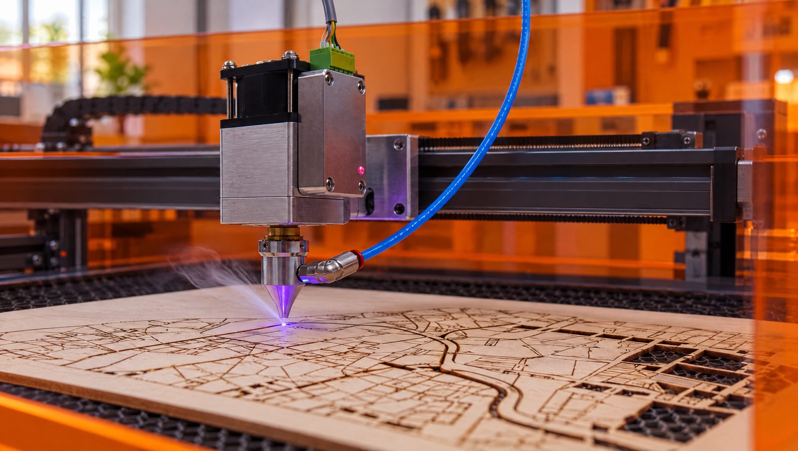An open-frame blue diode laser engraving and cutting a layered city map from thin plywood